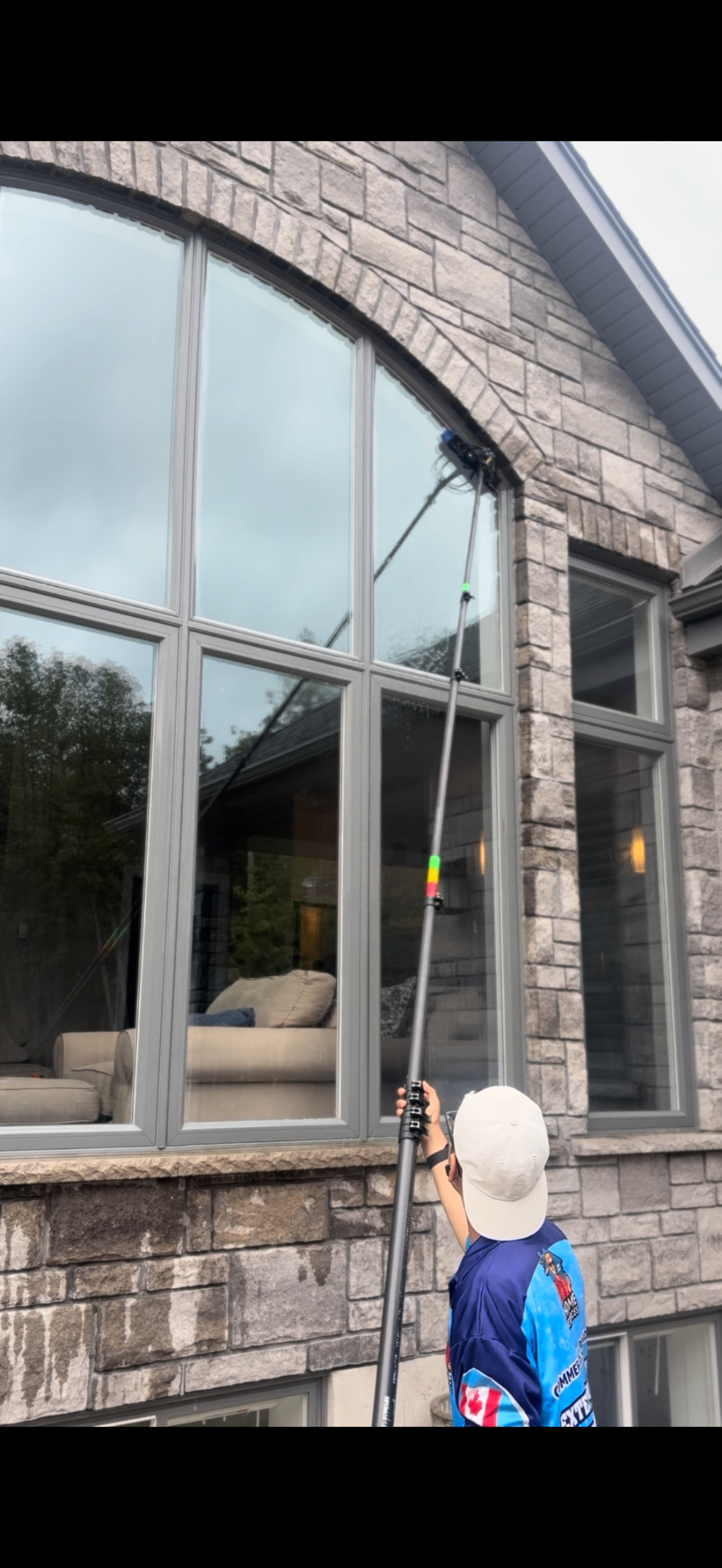 Water-fed pole cleaning a tall arched window on a stone home