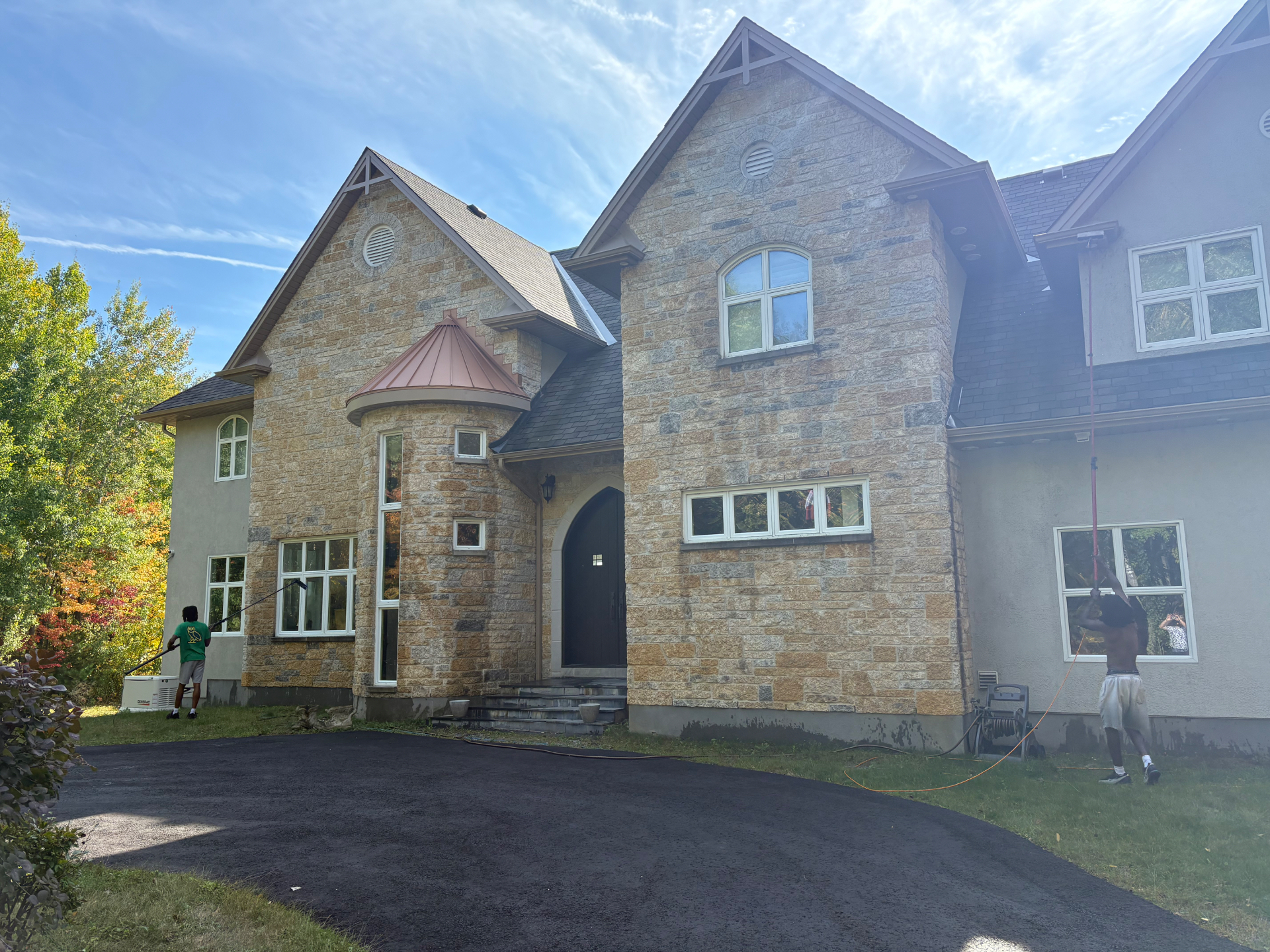 Two-person crew cleaning windows on a large stone home